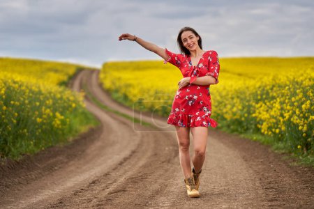 Portrait of a beautiful hispanic young woman in floral dress in a canola field at the end of the spring, in full bloom
