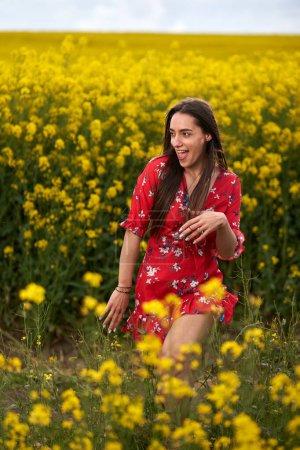 Foto de Retrato de una hermosa joven hispana en vestido floral en un campo de canola al final de la primavera, en plena floración - Imagen libre de derechos
