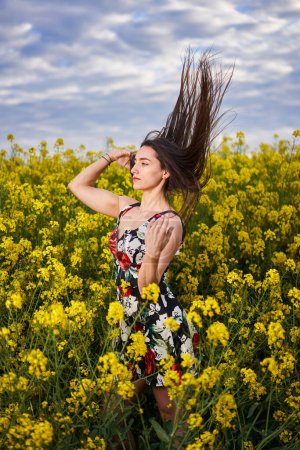 Téléchargez les photos : Portrait d'une belle jeune femme hispanique en robe florale dans un champ de canola à la fin du printemps, en pleine floraison - en image libre de droit