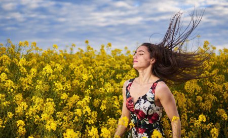 Photo for Portrait of a beautiful hispanic young woman in floral dress in a canola field at the end of the spring, in full bloom - Royalty Free Image