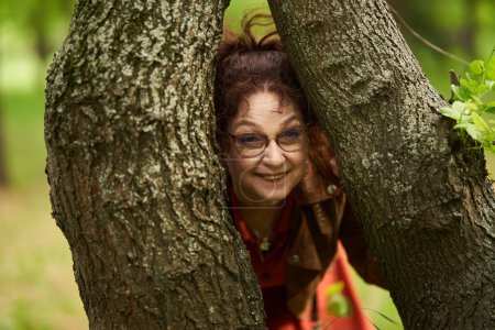 Foto de Juguetona mujer madura en el parque atascado entre dos árboles - Imagen libre de derechos