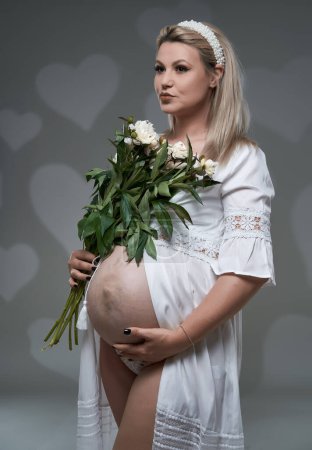 Photo for Beautiful pregnant young blonde woman in white gown on gray background - Royalty Free Image
