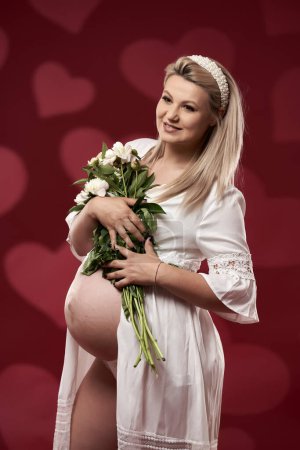 Téléchargez les photos : Belle jeune femme blonde enceinte en lingerie blanche sur fond rouge - en image libre de droit