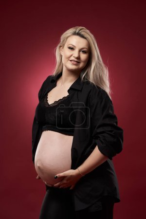 Photo for Beautiful pregnant young blonde woman in black lingerie on red background - Royalty Free Image