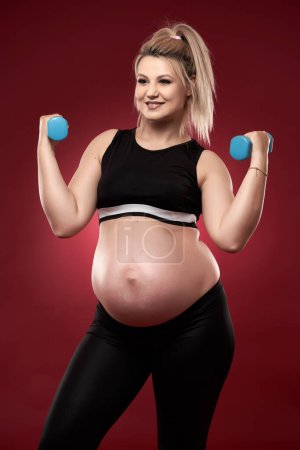 Photo for Young pregnant woman doing fitness exercises on red background, studio shot - Royalty Free Image