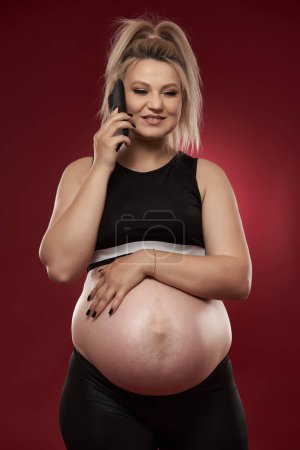 Photo for Pregnant woman speaking on mobile phone, studio shot on red background - Royalty Free Image