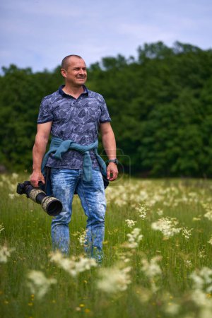 Photo for Professional nature photographer in the field by the forest, holding camera with a long telephoto lens - Royalty Free Image