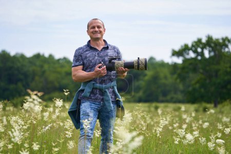 Photo for Professional nature photographer in the field by the forest, holding camera with a long telephoto lens - Royalty Free Image