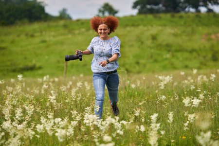Téléchargez les photos : Femme photographe de nature heureux et joyeux, courir avec un appareil photo sur une prairie - en image libre de droit