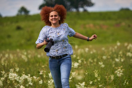 Téléchargez les photos : Femme photographe de nature heureux et joyeux, courir avec un appareil photo sur une prairie - en image libre de droit