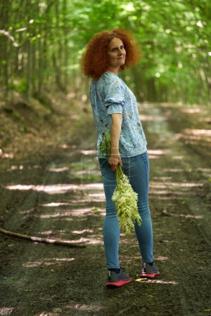 Téléchargez les photos : Portrait d'une femme rousse aux cheveux bouclés sur une prairie dans une forêt de chênes - en image libre de droit