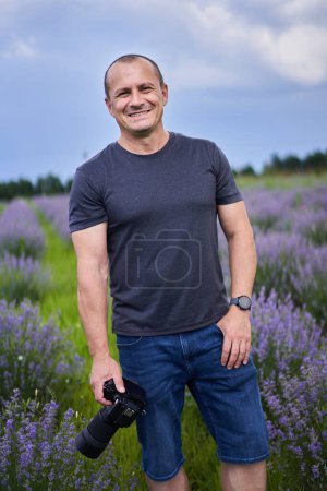 Photo for Professional nature photographer with camera shooting in a beautiful blooming lavender field in July - Royalty Free Image