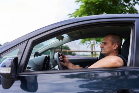 Foto de Hombre mensajes de texto en el teléfono móvil al volante de su coche en el verano - Imagen libre de derechos