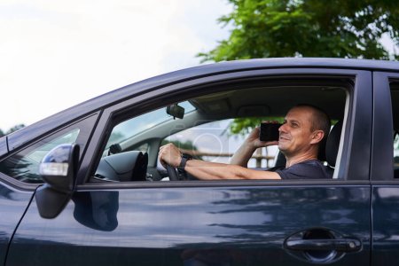 Téléchargez les photos : Homme utilisant un téléphone portable au volant de sa voiture en été - en image libre de droit