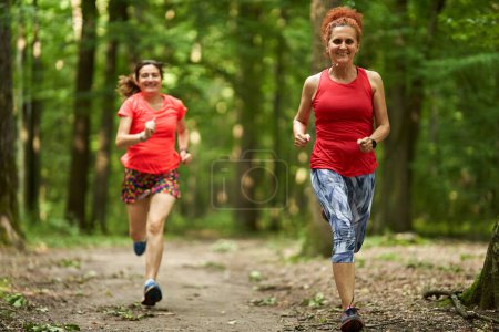 Photo for Two happy and healthy women running on a jogging trail in the forest - Royalty Free Image
