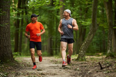 Foto de Dos amigos varones corriendo juntos por un sendero a través del bosque - Imagen libre de derechos