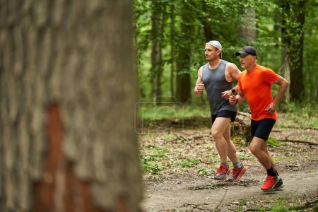 Photo for Two male friends running together on a trail through the forest - Royalty Free Image