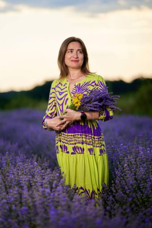 Photo for Attractive woman in a floral dress in a lavender field at sunset - Royalty Free Image