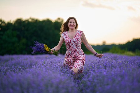 Photo for Attractive woman in a floral dress in a lavender field at sunset - Royalty Free Image