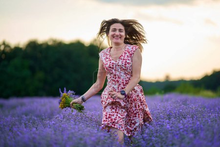 Téléchargez les photos : Belle femme dans une robe florale dans un champ de lavande au coucher du soleil - en image libre de droit