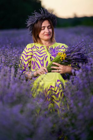 Téléchargez les photos : Femme avec une tiare de fleurs et un bouquet assis dans un champ de lavande - en image libre de droit