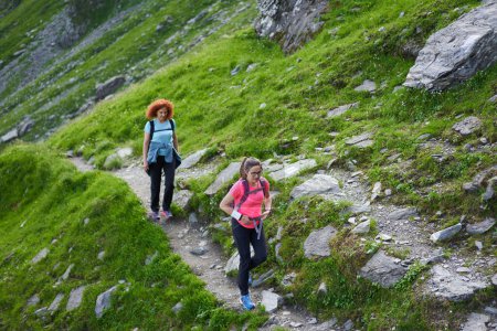 Foto de Dos mujeres excursionistas con mochilas senderismo en un sendero en las montañas rocosas - Imagen libre de derechos