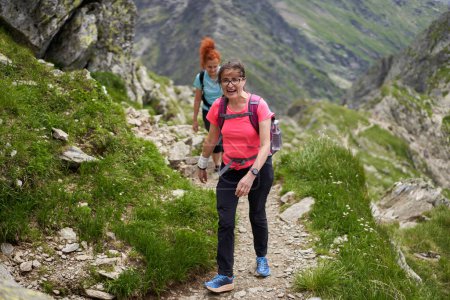 Téléchargez les photos : Deux randonneuses avec sacs à dos randonnée sur un sentier dans les montagnes rocheuses - en image libre de droit