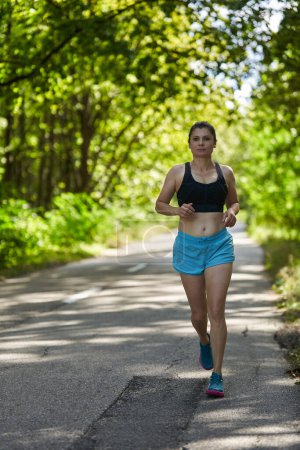 Téléchargez les photos : Femme coureuse jogging sur route asphaltée en forêt - en image libre de droit
