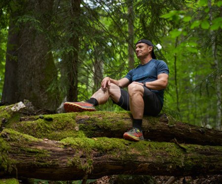 Téléchargez les photos : Homme assis sur un tronc d'arbre couvert de mousse après une randonnée - en image libre de droit