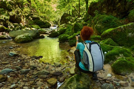 Photo for Woman hiker with backpack exploring wild gorges by a river with rapids and huge moss covered boulders - Royalty Free Image