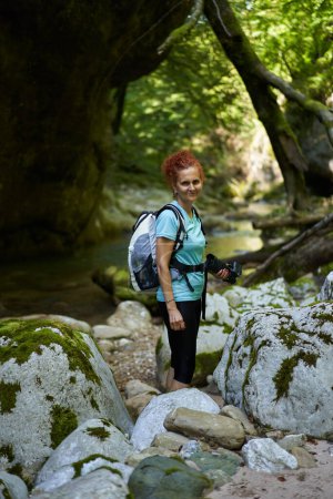 Téléchargez les photos : Femme randonneuse avec sac à dos explorant les gorges sauvages au bord d'une rivière avec des rapides et d'énormes rochers couverts de mousse - en image libre de droit