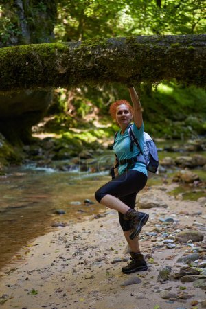 Téléchargez les photos : Femme randonneuse avec sac à dos explorant les gorges sauvages au bord d'une rivière avec des rapides et d'énormes rochers couverts de mousse - en image libre de droit