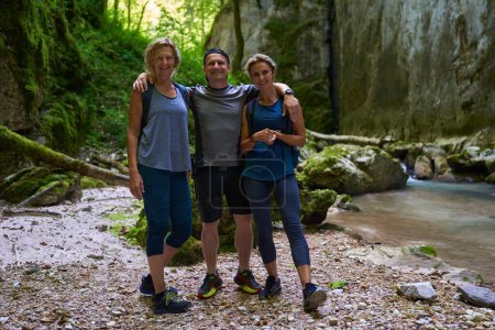 Photo for A man and two women hikers with backpacks posing for a photo in a gorge with a beautiful river - Royalty Free Image