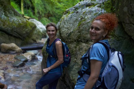 Foto de Mujeres excursionistas con mochilas explorando un exuberante cañón y un río - Imagen libre de derechos