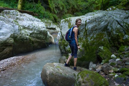 Foto de Mujer excursionista con mochila explorando un exuberante cañón con un río en él - Imagen libre de derechos