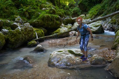 Foto de Mujer excursionista con mochila explorando un exuberante cañón con un río en él - Imagen libre de derechos