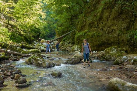 Téléchargez les photos : Randonneuses avec sacs à dos explorant un canyon luxuriant et une rivière - en image libre de droit