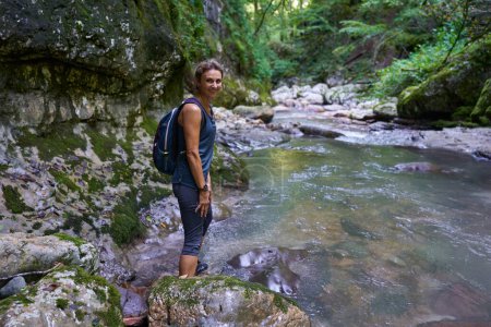 Téléchargez les photos : Femme randonneuse avec sac à dos explorant un canyon luxuriant avec une rivière dedans - en image libre de droit