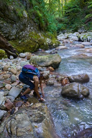 Téléchargez les photos : Femme randonneuse avec sac à dos explorant un canyon luxuriant avec une rivière dedans - en image libre de droit