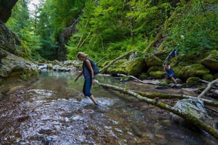 Téléchargez les photos : Randonneuses avec sacs à dos explorant un canyon luxuriant et une rivière - en image libre de droit