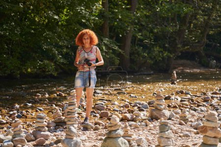 Téléchargez les photos : Femme photographe de nature tirant des tours de galets empilés sur un lit de rivière - en image libre de droit