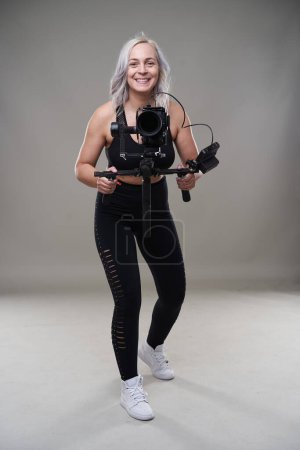 Photo for Woman videographer with cinema camera on gimbal on gray background - Royalty Free Image