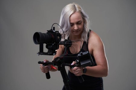 Foto de Mujer videógrafa con cámara de cine en gimbal sobre fondo gris - Imagen libre de derechos
