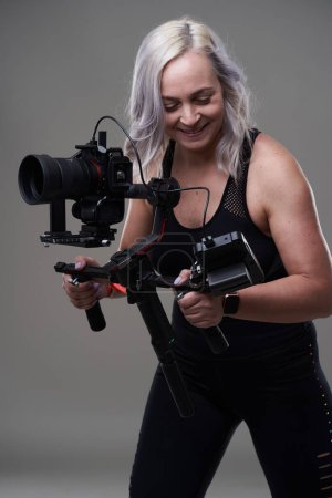 Téléchargez les photos : Vidéaste femme avec caméra cinéma sur cardan sur fond gris - en image libre de droit