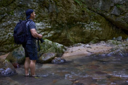 Téléchargez les photos : Photographe de nature professionnel avec sac à dos prenant des photos dans une gorge - en image libre de droit