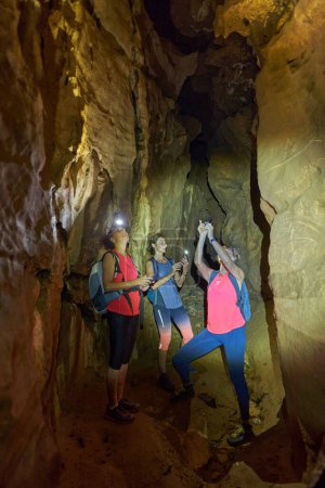 Foto de Tres mujeres con mochila explorando una cueva con antorchas en la cabeza - Imagen libre de derechos