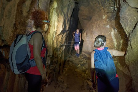 Foto de Tres mujeres con mochila explorando una cueva con antorchas en la cabeza - Imagen libre de derechos