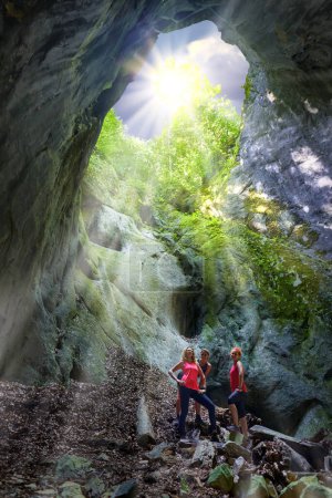Photo for Three women posing inside a cave with sun shining through above opening - Royalty Free Image