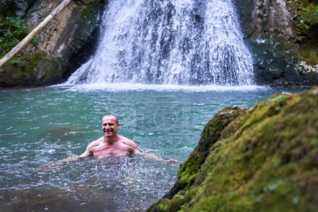 Téléchargez les photos : Homme athlétique fort se baignant dans une cascade avec de l'eau glacée de montagne - en image libre de droit