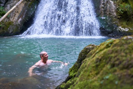 Téléchargez les photos : Homme athlétique fort se baignant dans une cascade avec de l'eau glacée de montagne - en image libre de droit